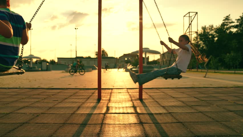 Children swinging on swings in city park, sunshine. Kids boy girl playing on swings, children flying, family weekend on swings. Active family, friends playing on summer playground, dreaming of flying.