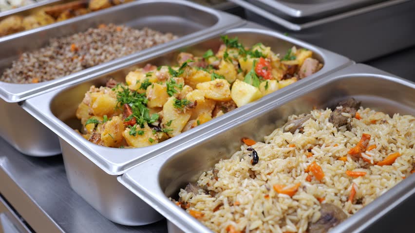 A close-up of metal containers with various ready meals in the dining room. Buckwheat, potatoes, pilaf. Meals served in the restaurant, dining room. Hot side dishes are served in the dining area.