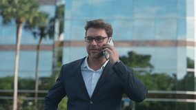 Male stock broker in a suit speaks on the phone near a modern glass office building. The scene symbolizes finance, inflation, and market turbulence stress and focus of global economic activity. - Powered by Shutterstock - Get 15% off with code: PIKWIZARD15