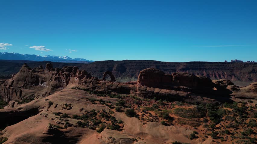 Aerial view of Delicate Arch, a sandstone arch with contrasting red rocks against a clear blue sky, Grand County, Grand County, United States.