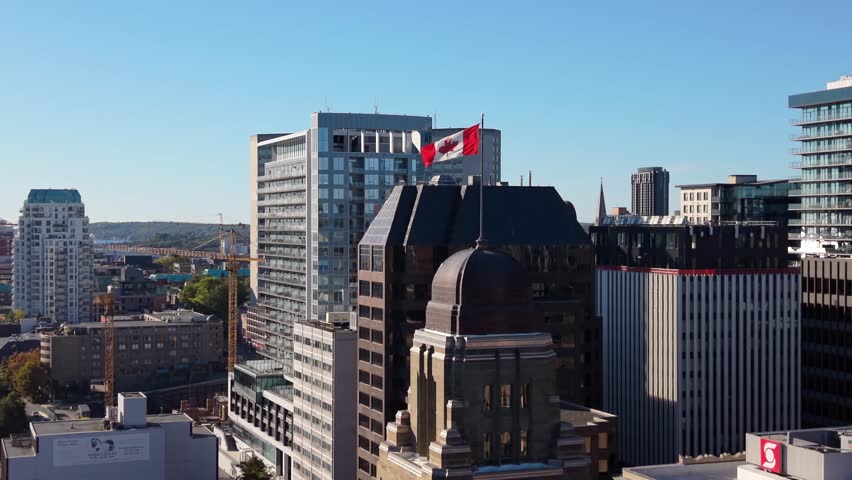 Aerial View Drone Shot Shows The Canadian Flag Prominently Flying Along Halifax Waterfront. The Vibrant Red And White Colors Contrast With The Ocean And Cityscape Below.