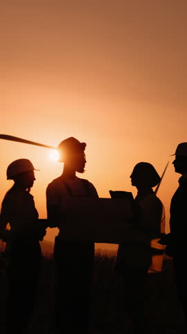 A group of people are silhouetted against a vibrant sunset, possibly discussing plans or projects. This vertical shot captures the essence of collaboration.