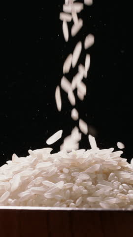 Cinematic Rice Texture - White Grains Falling Into Wooden Bowl on Black Background. Vertical shot.