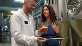 Cheerful male and female brewers discussing and tasting a new batch of craft beer while taking notes on a clipboard in a modern microbrewery with fermentation tanks in the background - Powered by Shutterstock - Get 15% off with code: PIKWIZARD15