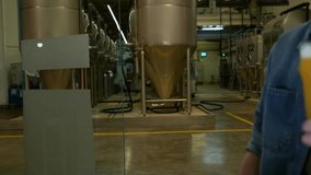 Close up of two people's hands clinking glasses of light and amber craft beer inside a modern brewery, with large stainless steel fermentation tanks visible in the blurred background - Powered by Shutterstock - Get 15% off with code: PIKWIZARD15