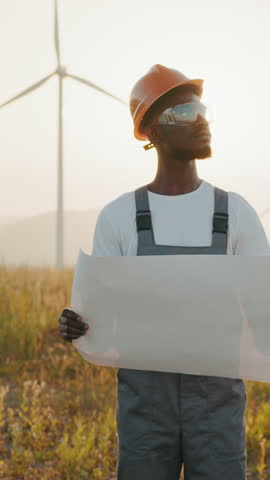 A construction worker in a hard hat examines a blueprint outdoors, bathed in sunlight. Vertical video.