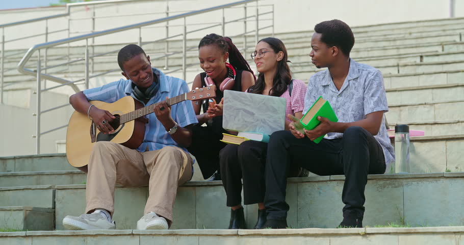 African young adult gen z man woman sitting on stair hold guitar play singing song together have fun joy outdoor place. Indian Happy smiling girl boy spend break time enjoy new day outside stairway 