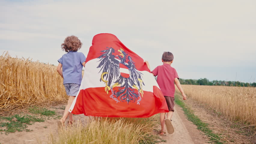 Children running with Austrian flag through golden wheat field under summer sky