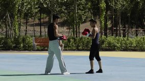Athletes in black and white sportswear with red boxing gloves standing face to face and boxing on outdoor court, green park background with shadows. - Powered by Shutterstock - Get 15% off with code: PIKWIZARD15