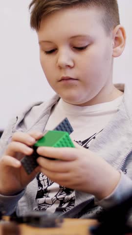 The boy of 11 years, plays in the designer from cubes, plates, circuits, wires. a small inventor creates robots, machines from different parts of the designer