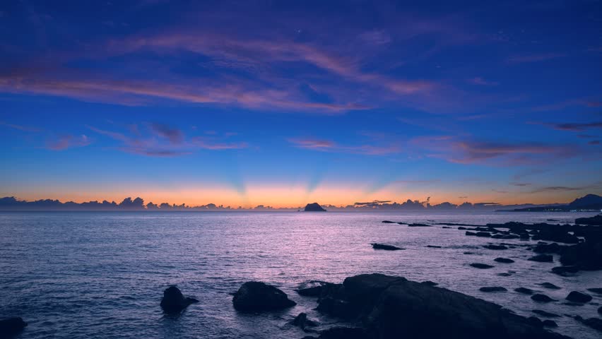 Stunning blue orange yellow sky before sunrise over Keelung Islet at Wanli New Taipei Taiwan, with calm waves in early autumn dawn.