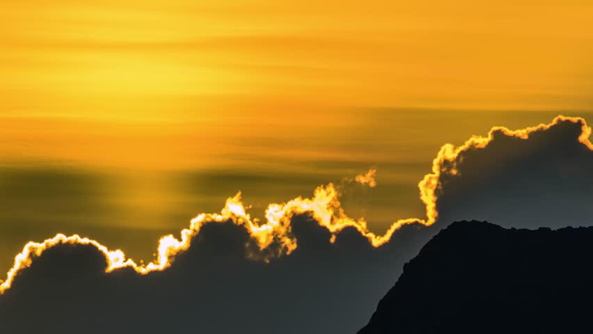 Sunrise emerging from clouds behind Keelung Islet at Wanli Taiwan, with orange yellow sky and calm waves in early autumn dawn.