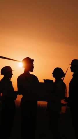 A team of people are silhouetted against a warm orange sunset, possibly discussing plans or working together outdoors.
