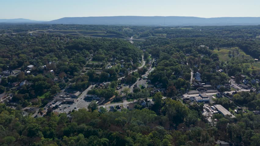 Experience panoramic views of Berkeley Springs, West Virginia, featuring lush greenery, historic homes, and serene landscapes under a clear blue sky.