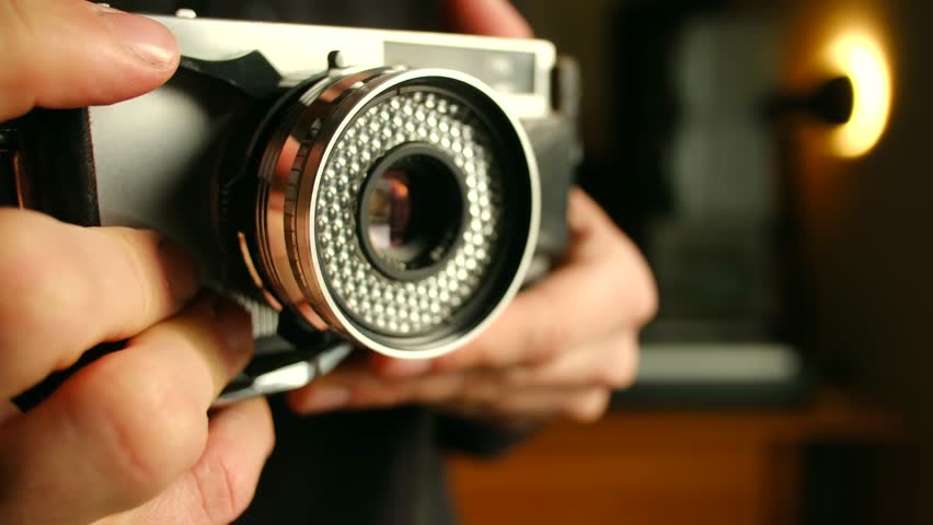 Photographer hands adjusting settings on classic vintage film camera, with lens aperture blades opening, closing in dimly lit warm environment. Photographer adjusting vintage film camera lens aperture