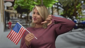Young blonde woman holds and gently waves united states flag on urban city street while smiling softly; pride. - Powered by Shutterstock - Get 15% off with code: PIKWIZARD15