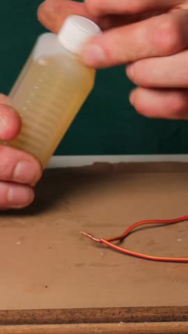 Man applies liquid to electrical wires before soldering with soldering iron. Preparing wires for soldering by applying flux. Flux application process for clean and strong wire connection. vertical vid