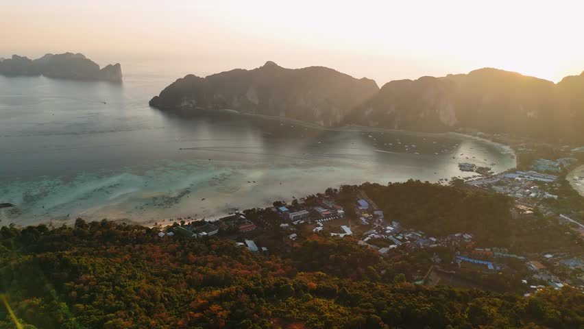 Golden sunset illuminating phi phi islands tropical coastline, revealing vibrant village nestled between azure waters and verdant landscape in thai archipelago, Thailand