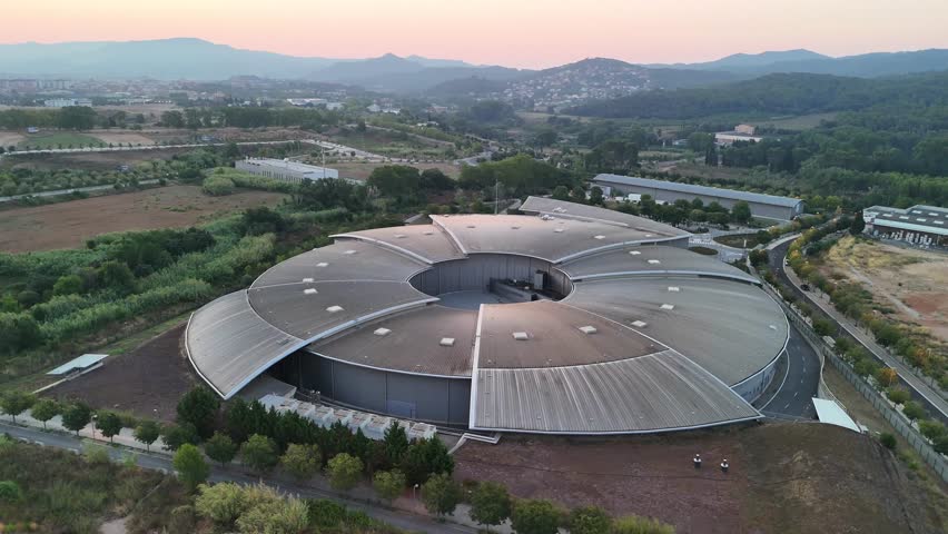 Aerial drone orbit around the ALBA Synchrotron particle accelerator in Cerdanyola, Spain. The footage captures the full circular architecture of the scientific research facility near Barcelona