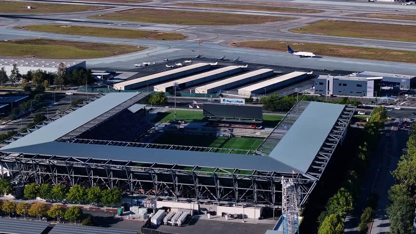 San Jose, United States - 09 October 2025: Aerial view of PayPal Park stadium with its green pitch, surrounded by trees and an airport runway in the background.
