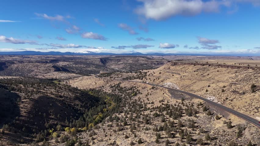 Aerial view of U.S. Highway 26 cutting through a landscape of canyons, plateaus, and scattered trees under a blue sky, Warm Springs, Oregon, United States.