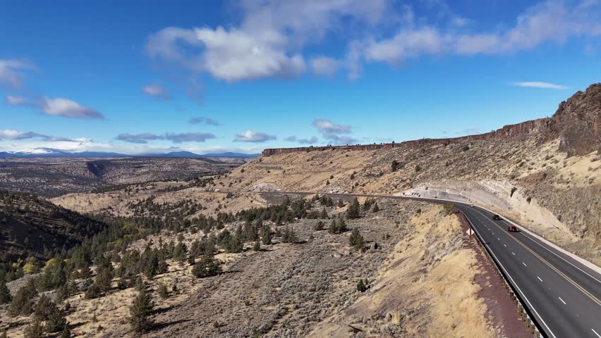Aerial view of U.S. Highway 26 winding through the arid landscape under a blue sky dotted with clouds, Warm Springs, Oregon, United States.