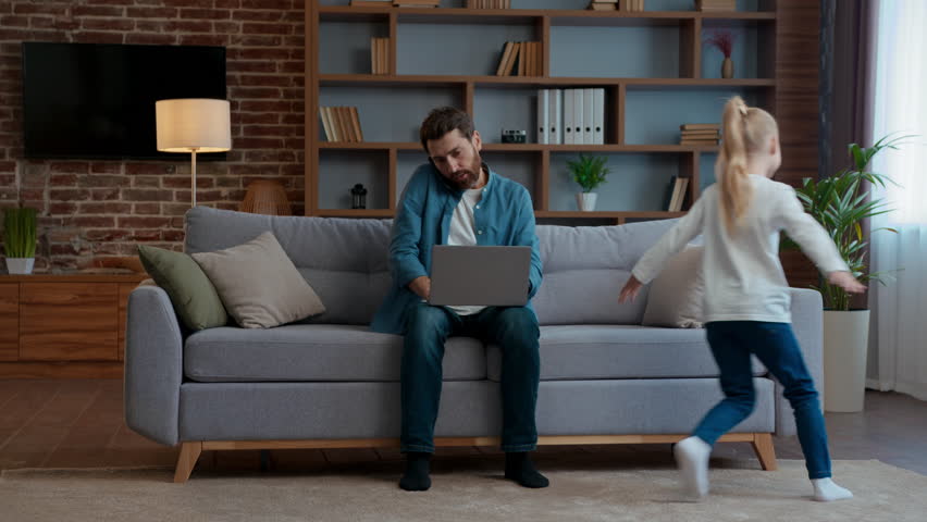 Family at home freelancer dad working laptop talking phone active child running around sofa hyperactive playful kid girl daughter run noisy disturbing father from multitasking work stressed parenting