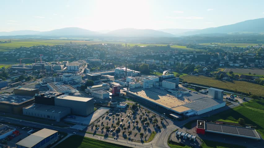 Orbe, Switzerland - 19 September 2025: Aerial view of the Nestle Product Technology Center nestled amid lush greenery, buildings, and distant mountains.