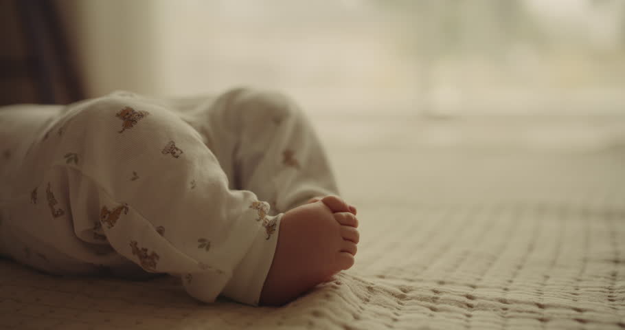 A detailed close-up of delicate small feet of a newborn baby boy, resting on a blanket by the window.