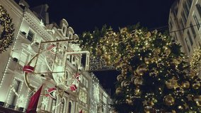 Elegant Christmas lights adorn a London street at night, showcasing a prominent Ferris wheel decoration, sparkling archways, and a richly decorated fir tree with golden baubles - Powered by Shutterstock - Get 15% off with code: PIKWIZARD15