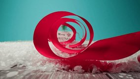 Vibrant red ribbon curls through artificial snow, leading to a charming Merry Christmas sign with a gnome figurine and a small Christmas tree on a blue background - Powered by Shutterstock - Get 15% off with code: PIKWIZARD15