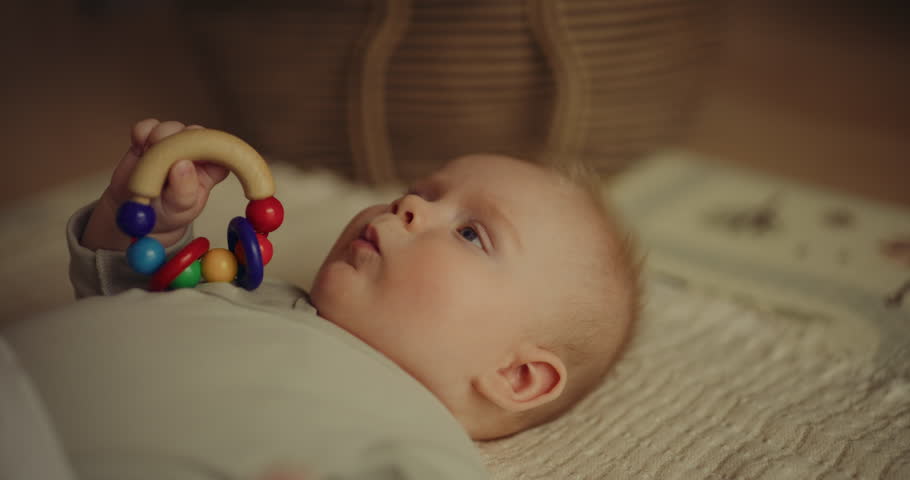 Cute baby boy lying on a blanket holding a wooden toy, capturing a heartwarming infant moment.