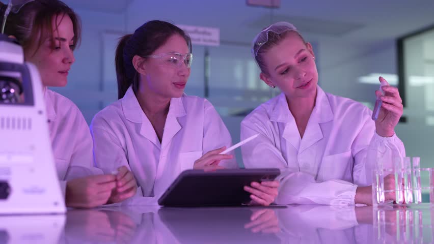 A diverse and happy team of young female scientists collaborates in a futuristic lab, discussing innovative ideas and reviewing research data together on a digital tablet. - Powered by Shutterstock - Get 15% off with code: PIKWIZARD15