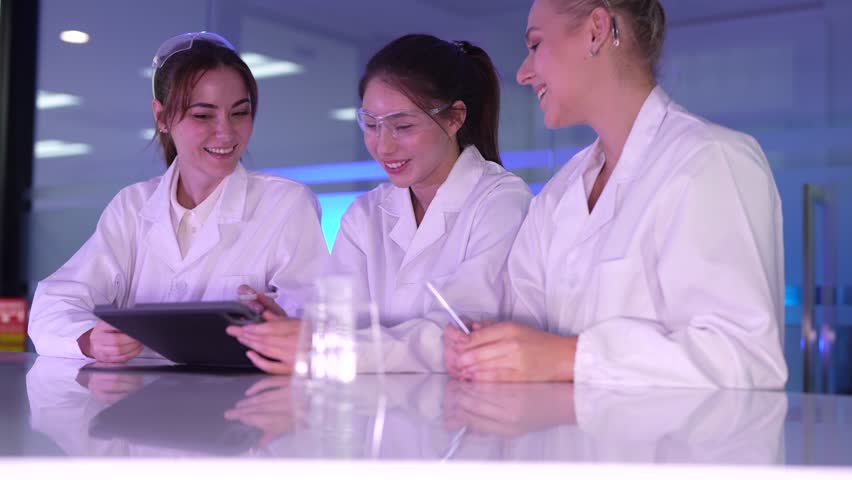 A diverse and happy team of young female scientists collaborates in a futuristic lab, discussing innovative ideas and reviewing research data together on a digital tablet. - Powered by Shutterstock - Get 15% off with code: PIKWIZARD15