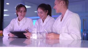 A diverse and happy team of young female scientists collaborates in a futuristic lab, discussing innovative ideas and reviewing research data together on a digital tablet. - Powered by Shutterstock - Get 15% off with code: PIKWIZARD15
