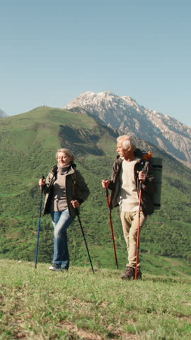 Slow motion vertical video elderly couple hiking with poles in mountains active lifestyle wellness healthy aging fitness retirement outdoor activity freedom longevity wellbeing nature