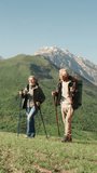 Slow motion vertical video elderly couple hiking with poles in mountains active lifestyle wellness healthy aging fitness retirement outdoor activity freedom longevity wellbeing nature - Powered by Shutterstock - Get 15% off with code: PIKWIZARD15