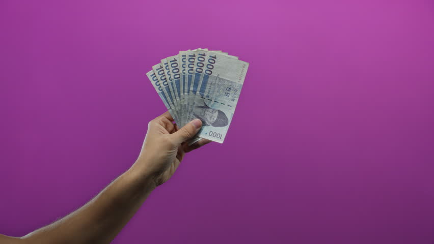 Man holding south korean won banknotes against a vibrant purple wall, highlighting economic themes with a simple isolated background.