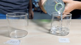 Person pours cold water into labeled glass beaker under bright indoor lighting, static camera view - Powered by Shutterstock - Get 15% off with code: PIKWIZARD15