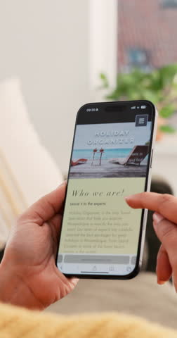 Hands, online booking and phone screen with person on sofa in living room of home for planning. Hospitality, scrolling and vacation with woman in apartment to search for luxury accommodation