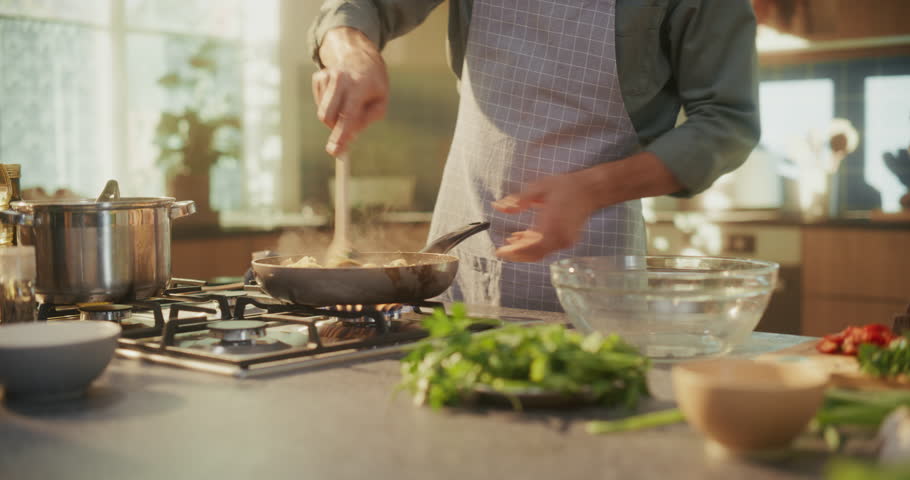 Close Up of a Man in Apron Cooking a Steaming Pasta Meal with Shrimps, Seafood, Vegetables in a Frying Pan in a Modern Kitchen, Preparing a Tasty Dish in a Home Kitchen
