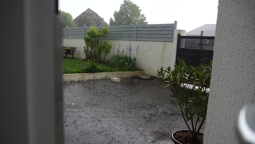 A hailstorm hits a terraced house. The terrace is covered in rain and the plants are wet.
