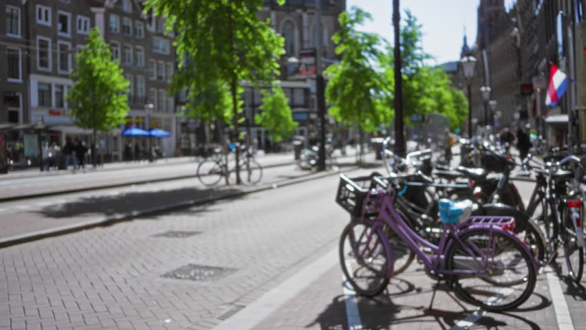 Bicycles in blurred amsterdam street scene with trees and buildings creating a bokeh effect under a sunny sky in the netherlands.