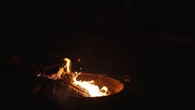 Night campfire with logs in metal fire pit, flames glowing in shades of yellow, orange, blue, and green against complete darkness - Powered by Shutterstock - Get 15% off with code: PIKWIZARD15