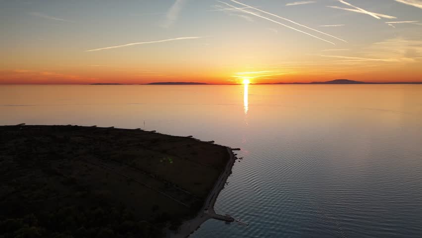Drone flying backwards over the Adriatic Sea at sunset near Pag Island, Croatia. Calm and romantic golden light reflecting over tranquil evening waters.