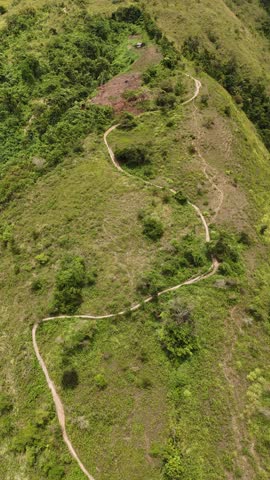 Aerial drone view of a hiking trail winding through the green mountain ridge. The scenic path leads to the summit, surrounded by lush tropical vegetation and natural landscape.