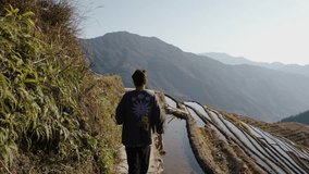 A traveler walks along a narrow path beside flooded rice terraces in Longsheng, Guangxi, China - Powered by Shutterstock - Get 15% off with code: PIKWIZARD15