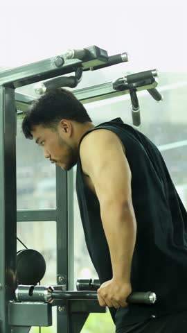 Athletic man performs assisted pull-up exercise in bright modern gym, showcasing upper body strength.