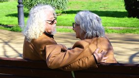 Happy senior couple sitting close together on park bench, hugging and looking at each other with love and joy. Elderly man and woman in brown jackets enjoying romantic moment outdoors. - Powered by Shutterstock - Get 15% off with code: PIKWIZARD15