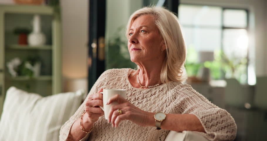Home, thinking and old woman on sofa, coffee and memory with break, relax and caffeine in living room. Wonder, pensioner or senior person on couch, herbal tea or nostalgia with reflection or remember
